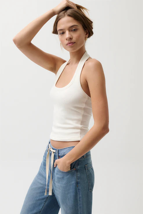 Woman wearing a white halter top and blue jeans on a plain background
