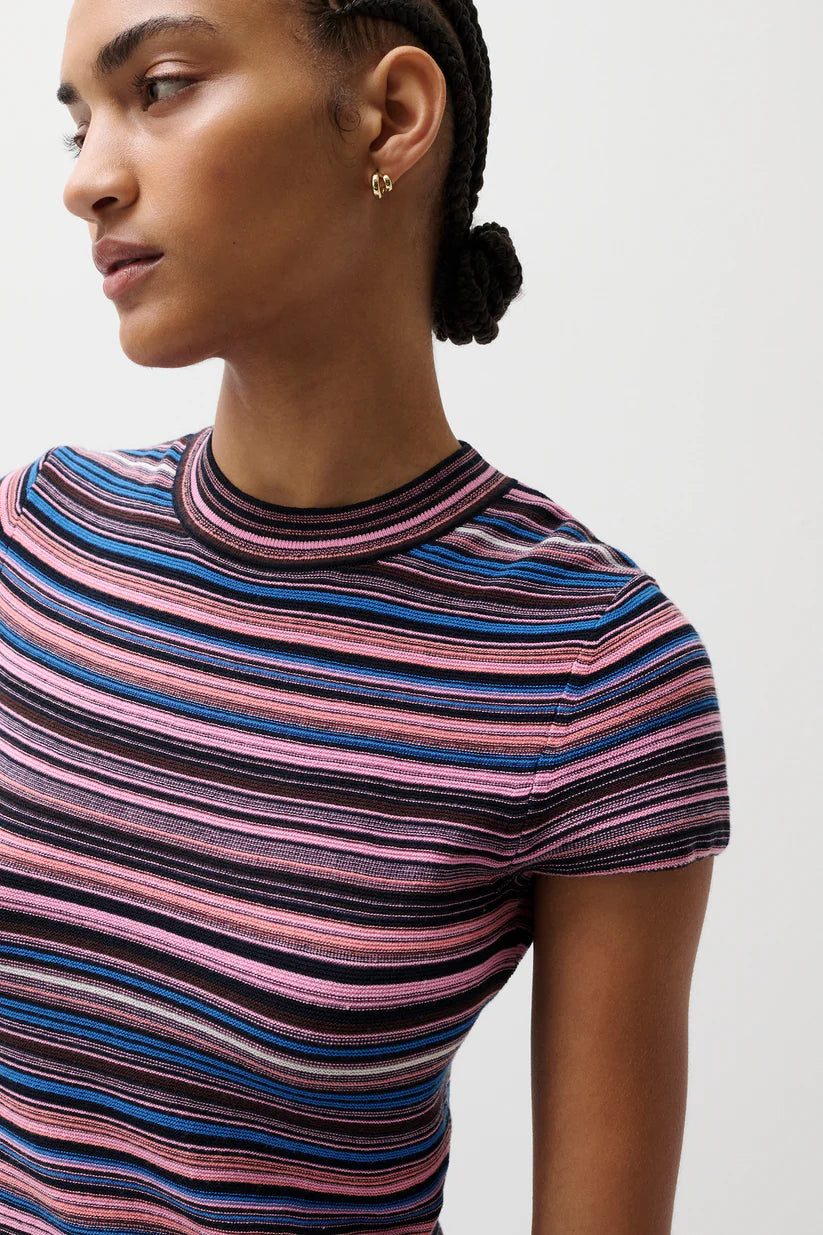 Woman wearing a striped shirt with pink, blue, and black colors on a plain background