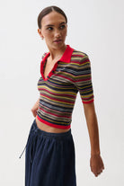 Woman wearing a colorful striped polo shirt and dark pants on a white background