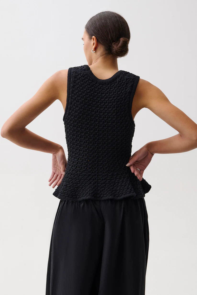 Woman wearing a black sleeveless top and black pants against a white background
