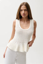 Woman wearing a white crochet tank top against a plain background