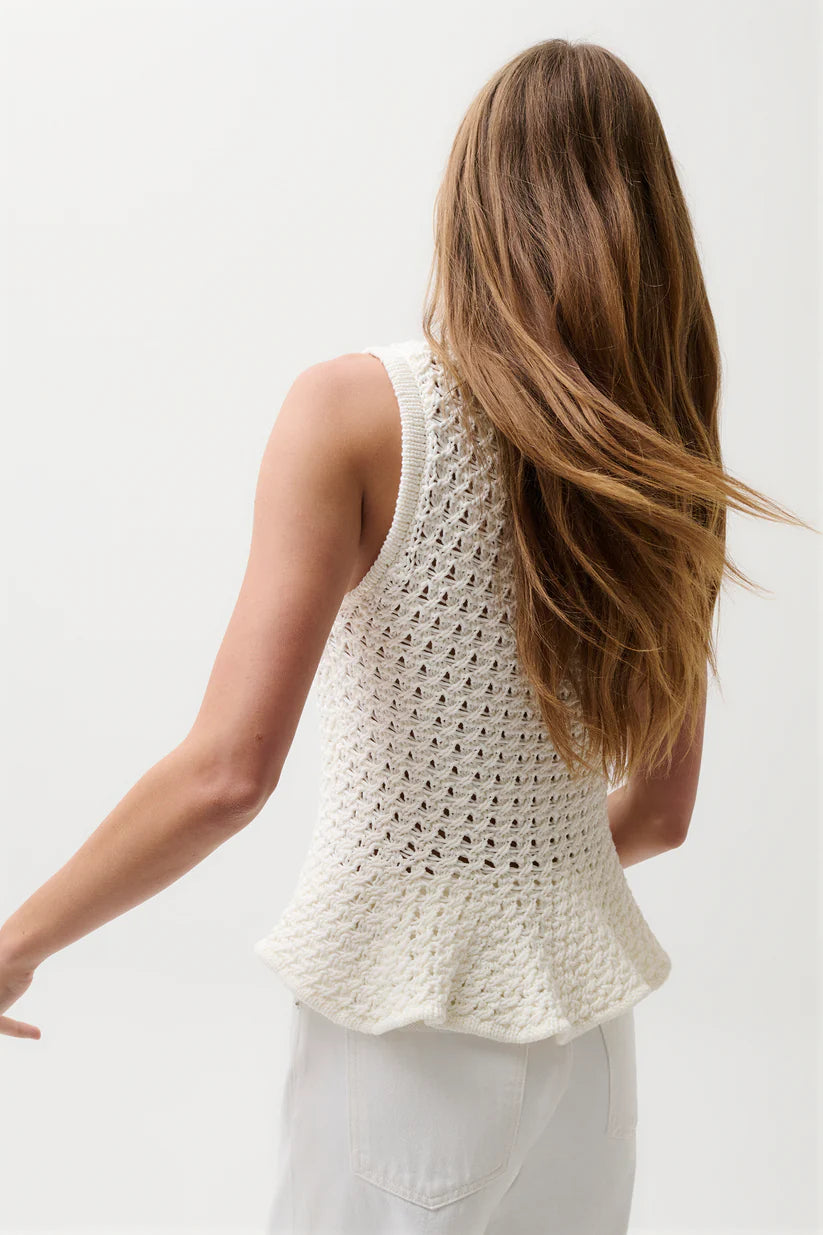 Woman wearing a white crochet sleeveless top against a plain background