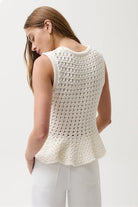 Woman wearing a white crochet sleeveless top against a plain background