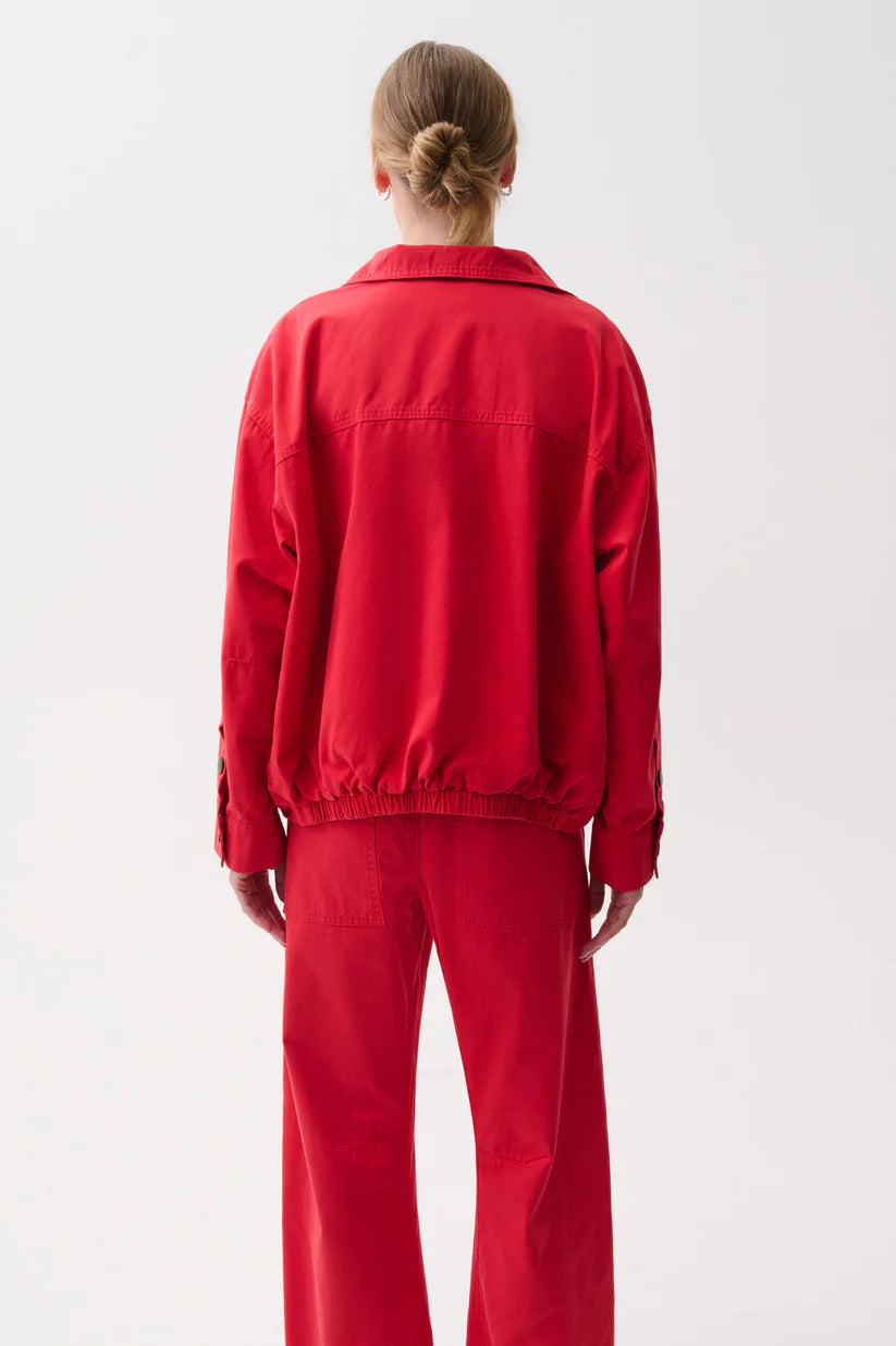 A model viewed from behind wearing a bright red jacket and matching red trousers against a plain white studio background.