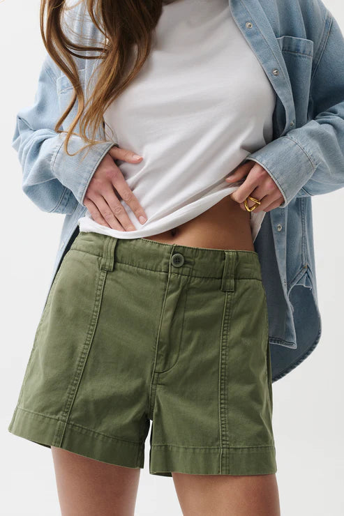 Person wearing green shorts, a white top, and a light blue denim jacket on a plain background