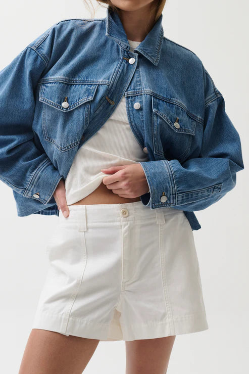 Person wearing a blue denim jacket and white shorts on a plain background