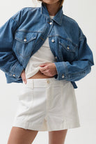 Person wearing a blue denim jacket and white shorts on a plain background