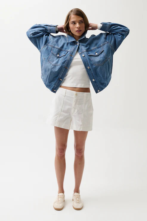 Woman wearing a blue denim jacket, white top, and shorts on a white background