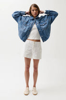 Woman wearing a blue denim jacket, white top, and shorts on a white background