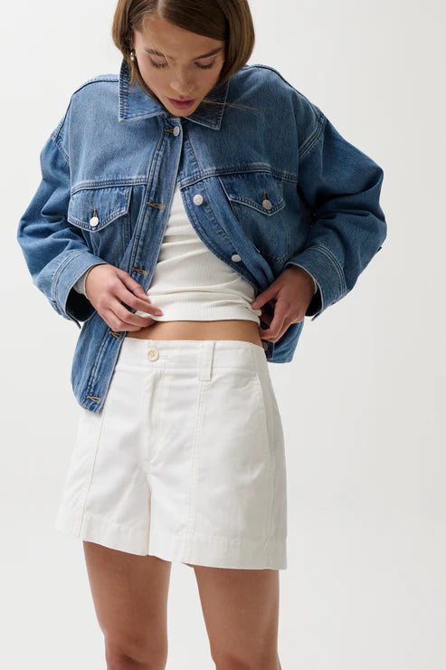Person wearing a blue denim jacket and white skirt on a plain background