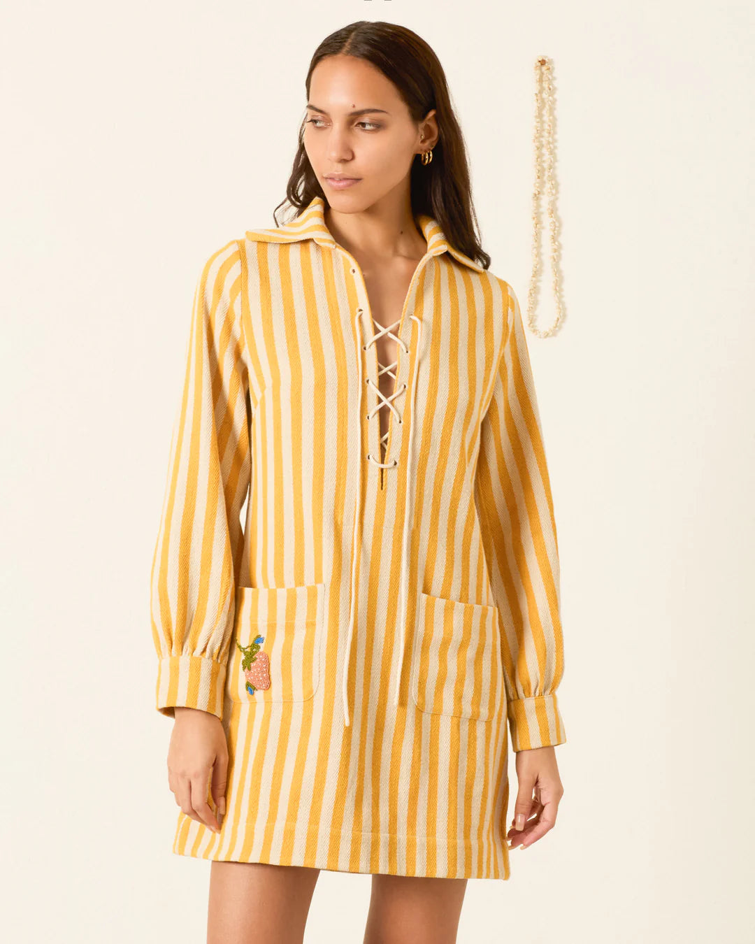 Woman wearing a yellow and white striped dress with a lace-up front on a beige background