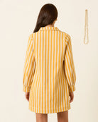 Woman wearing a yellow and white striped dress against a beige background