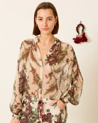 Woman wearing a floral blouse with a matching skirt, standing next to a red floral bag on a beige background.