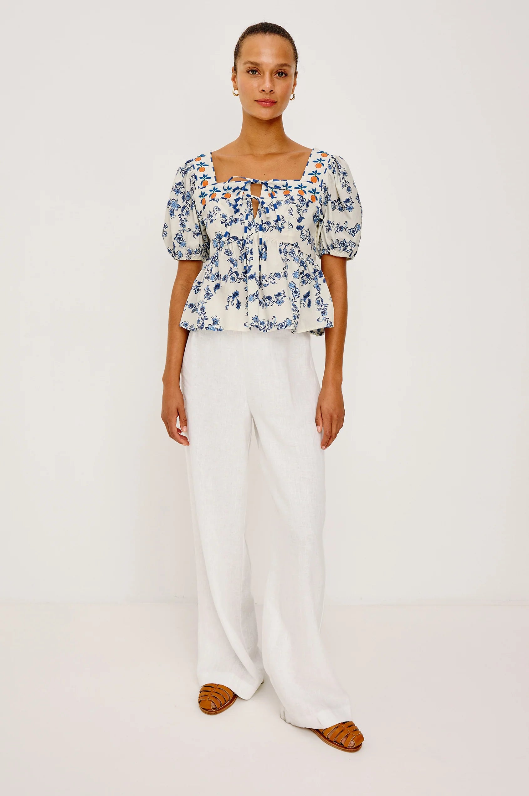 Woman wearing a floral blouse and white pants on a plain background