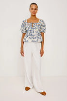 Woman wearing a floral blouse and white pants on a plain background