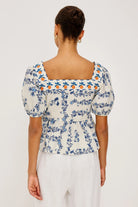 Woman wearing a floral blouse with puff sleeves on a plain background