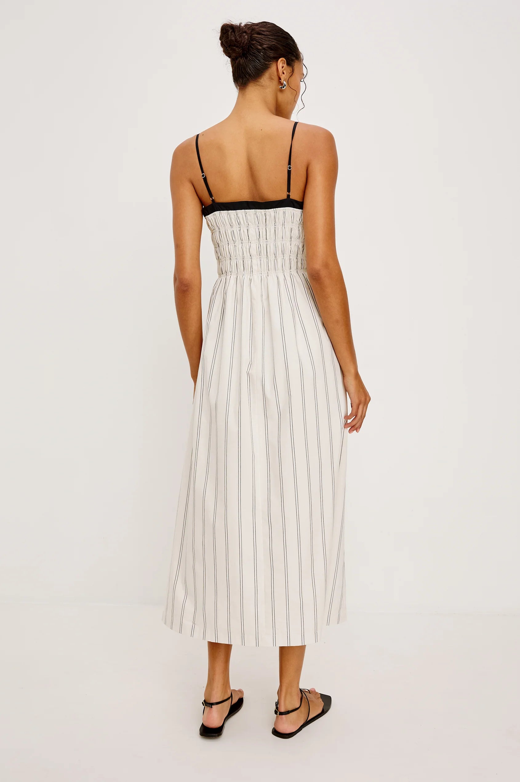 Woman wearing a white pleated dress with black straps on a white background