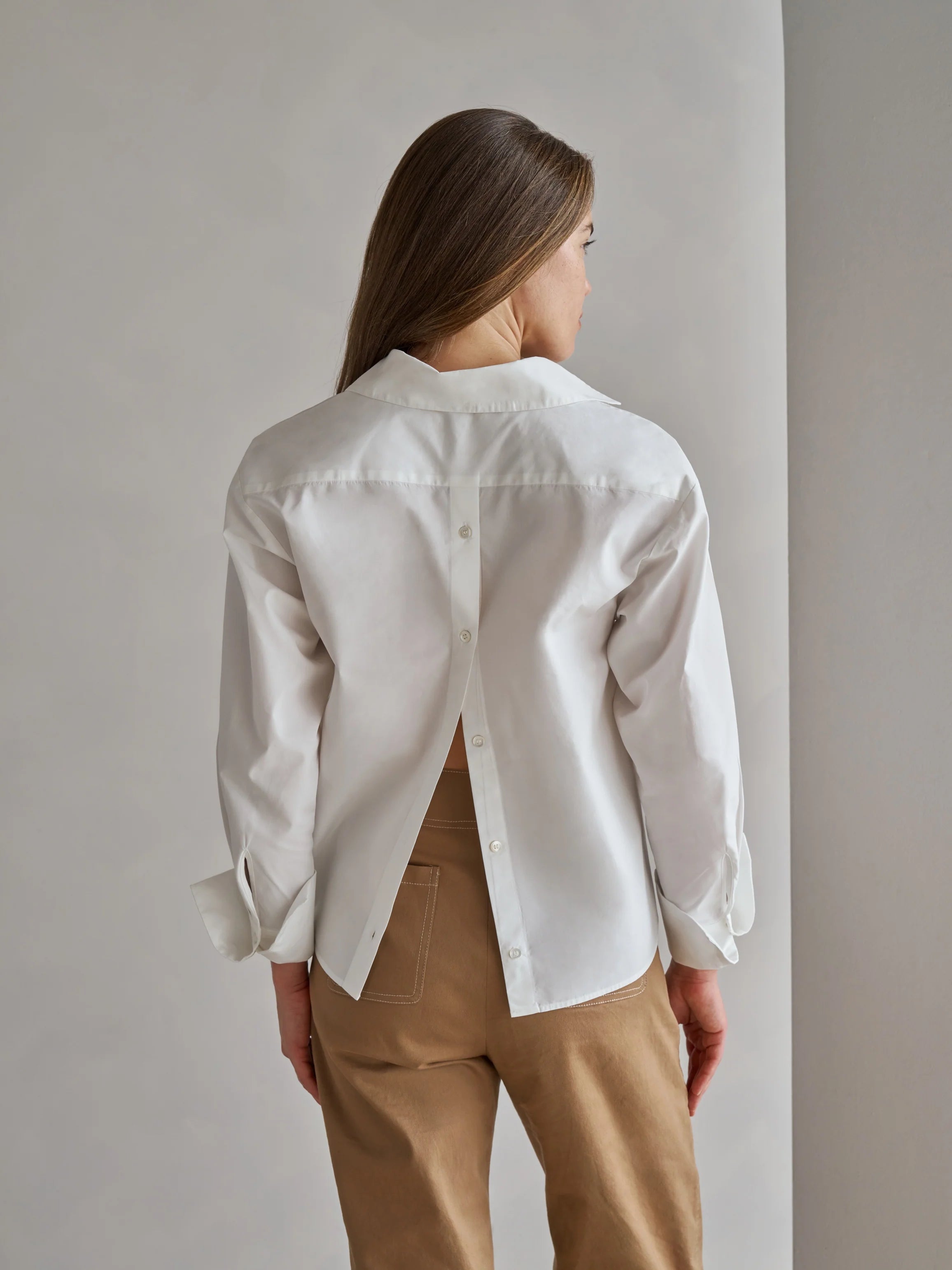 Person wearing a white shirt and brown pants against a plain background