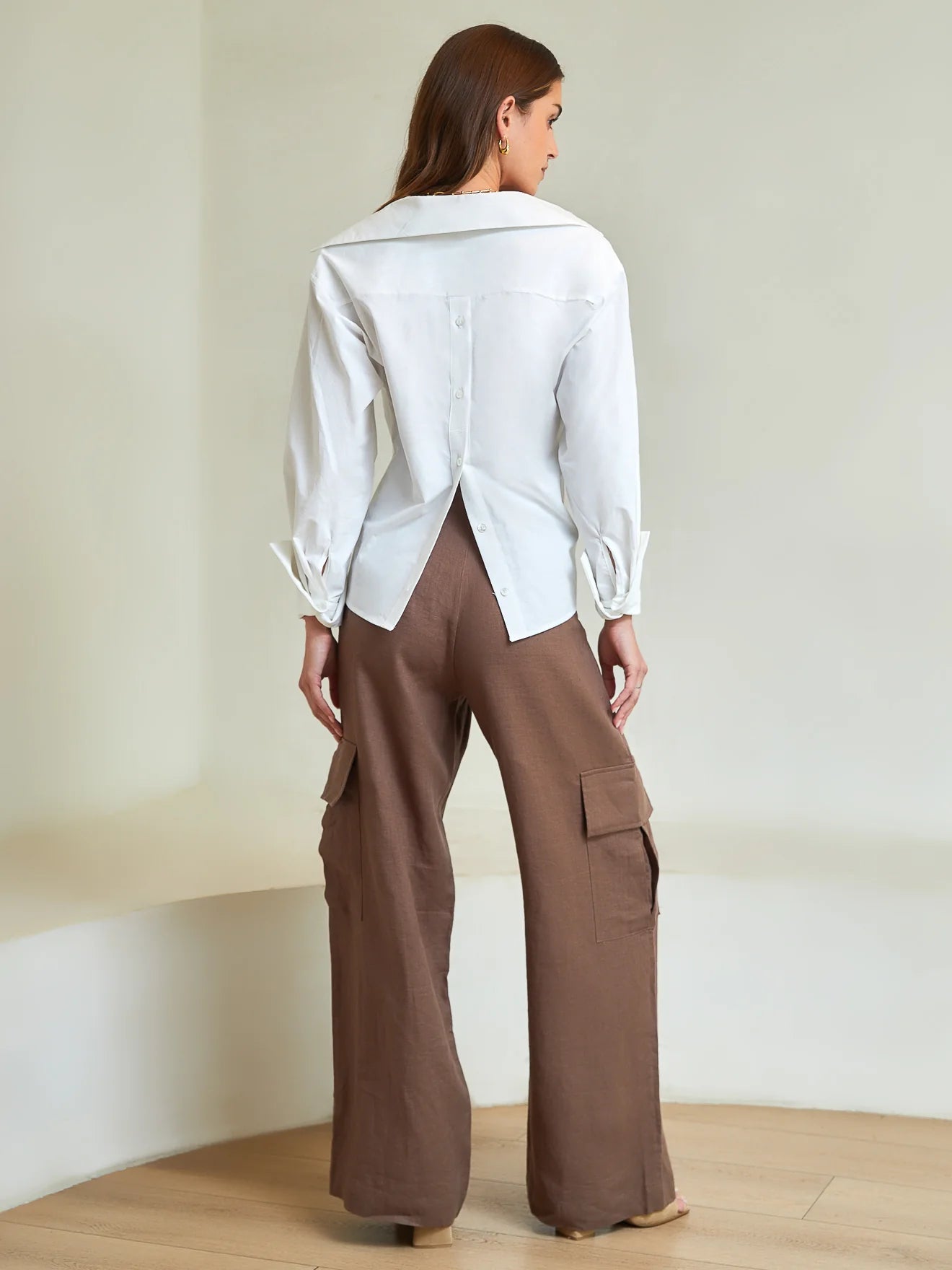 Woman wearing a white shirt and brown cargo pants in a minimalistic setting