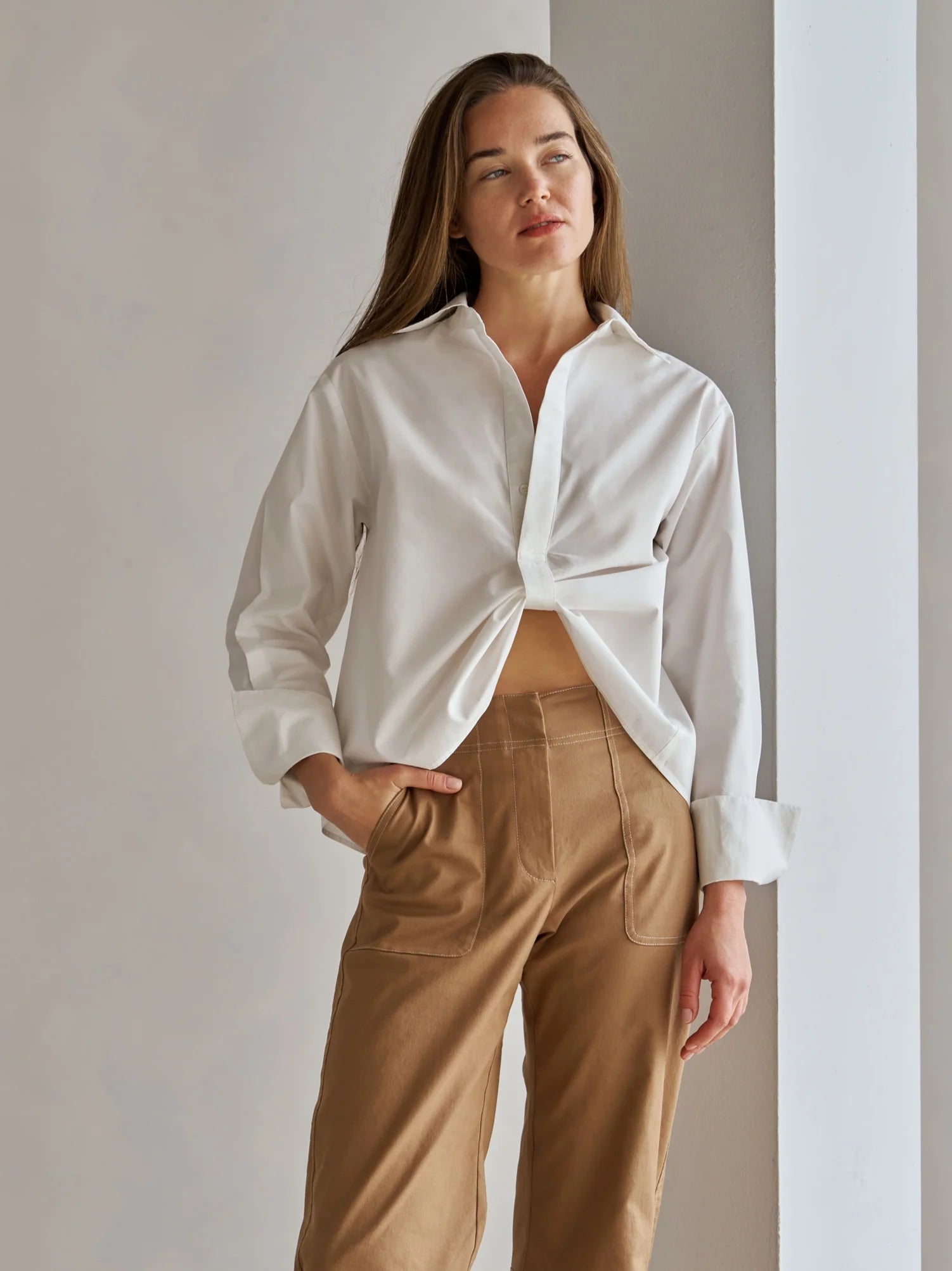 Woman wearing a white shirt and brown pants against a neutral background