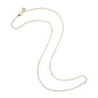 A delicate gold chain necklace with small, evenly spaced clear round beads, displayed on a clean white background. It features a lobster clasp and an adjustable extender chain with a circular brand tag engraved with 'AN'.