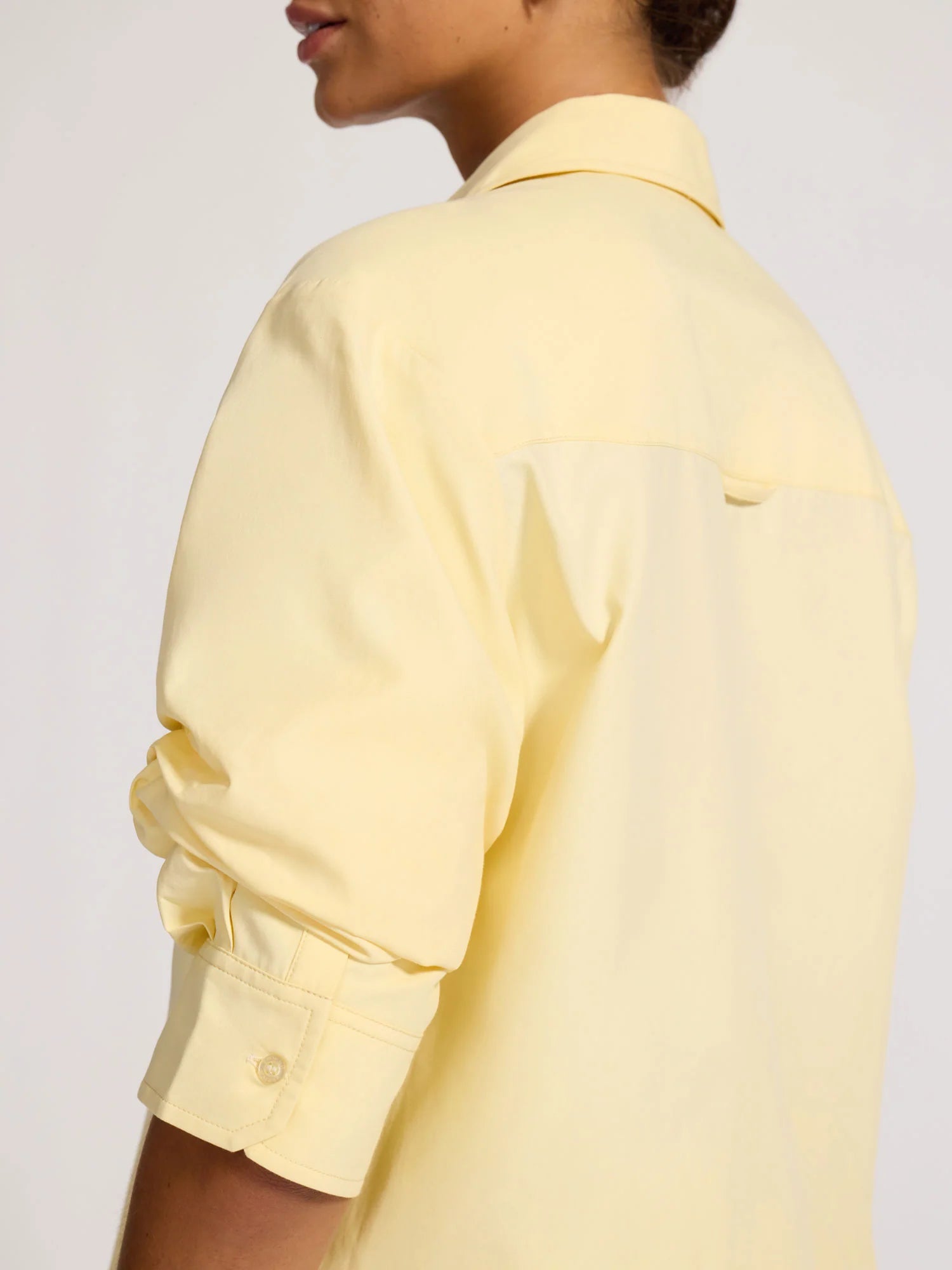 Person wearing a light yellow shirt against a plain background