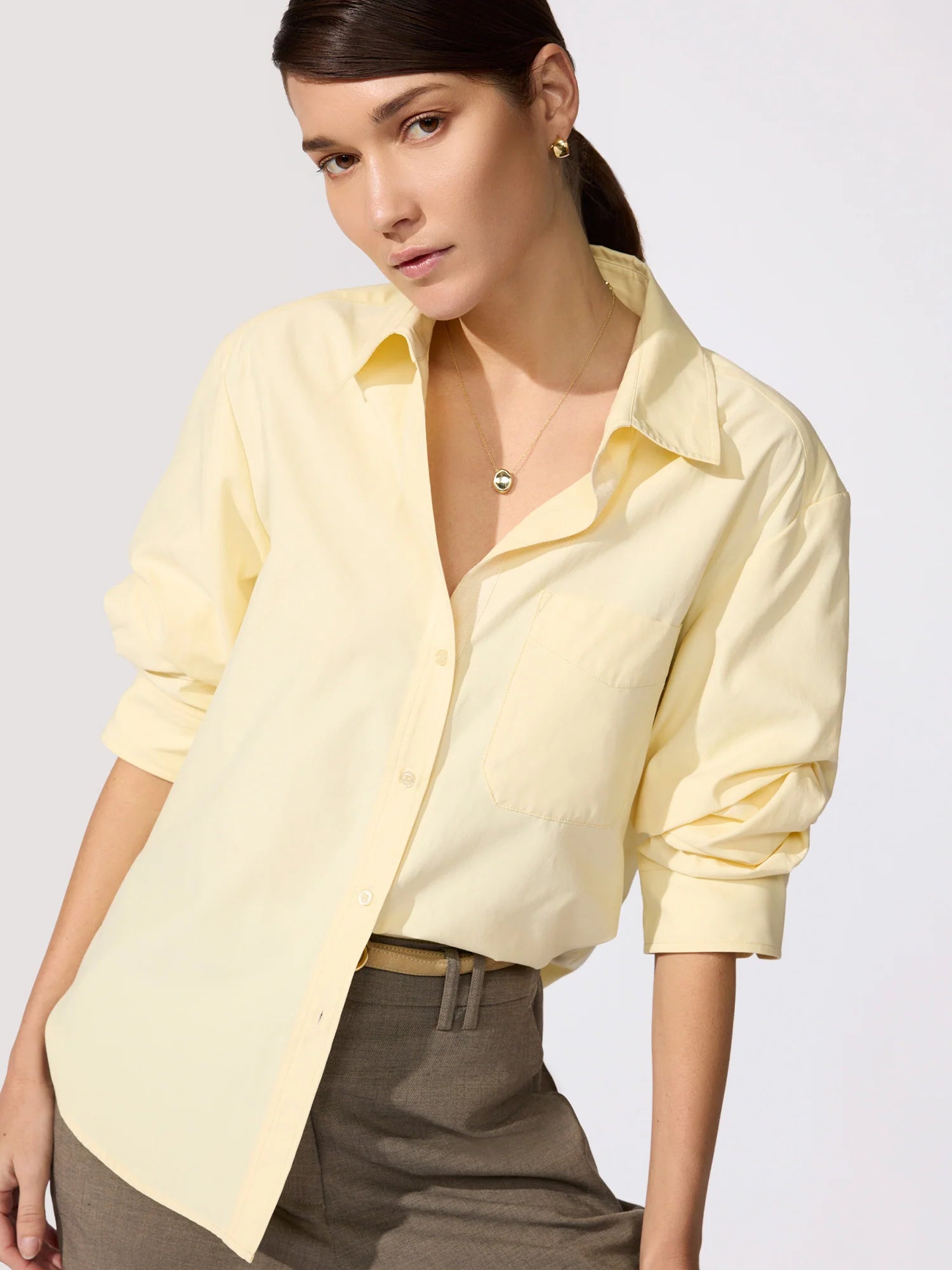 Woman wearing a light yellow shirt with rolled-up sleeves on a plain background