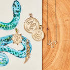 Gold snake-themed jewelry on a wooden surface with a painted snake design.