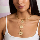 Woman wearing gold necklaces with circular pendants on a plain background