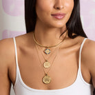Woman wearing a gold necklace with intricate pendants against a light background