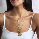 Woman wearing a white tank top with gold necklaces featuring circular pendants.