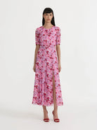 A model wearing a pink short-sleeved midi dress with a red and white floral pattern, standing against a plain white studio background.