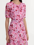 A woman wearing a short-sleeve pink floral dress with a matching waist tie, shown from the neck down against a plain light background.