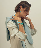 Woman wearing a light blue jacket and beige outfit with turquoise accessories against a neutral background