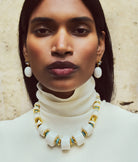 Woman wearing a white turtleneck sweater and a necklace with large white beads and gold accents.