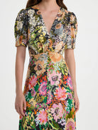 A woman wearing a short puff-sleeve wrap dress with a vibrant multicolor floral print on a light gray background.