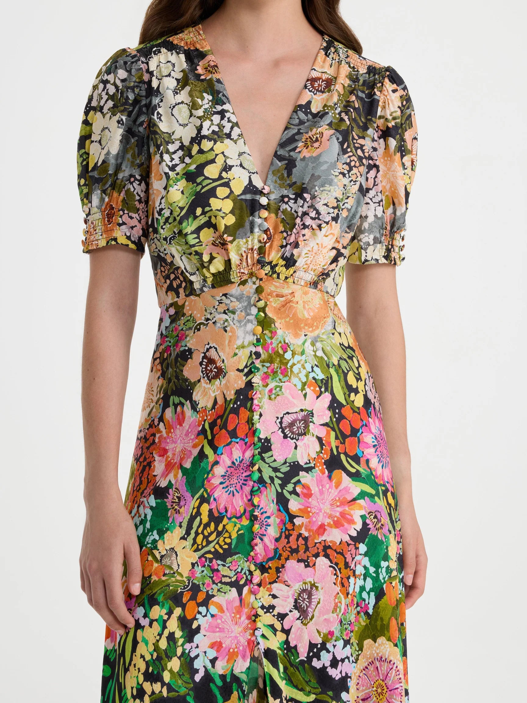 A woman wearing a short puff-sleeve wrap dress with a vibrant multicolor floral print on a light gray background.
