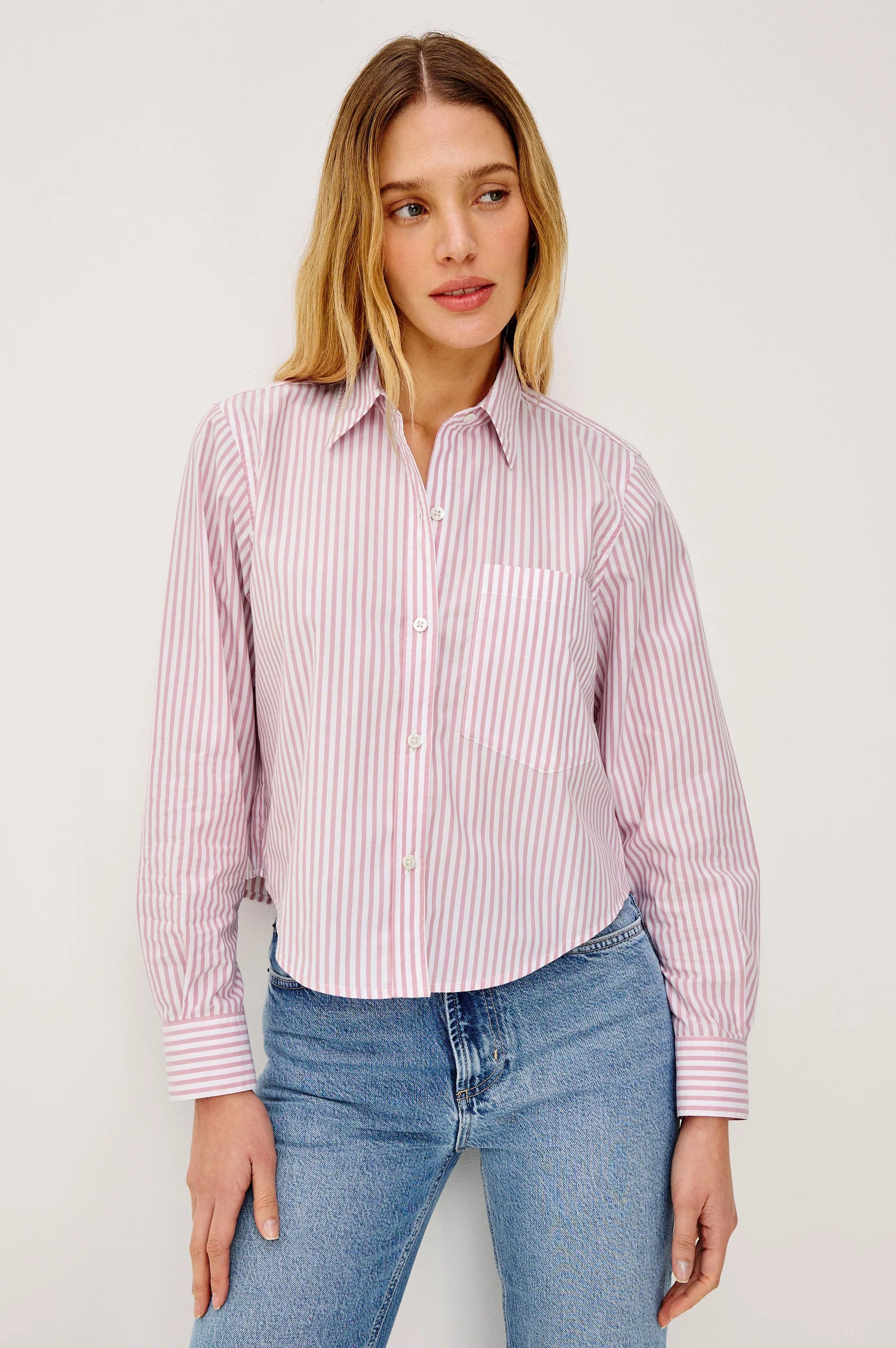 Woman wearing a pink and white striped shirt with blue jeans on a plain background