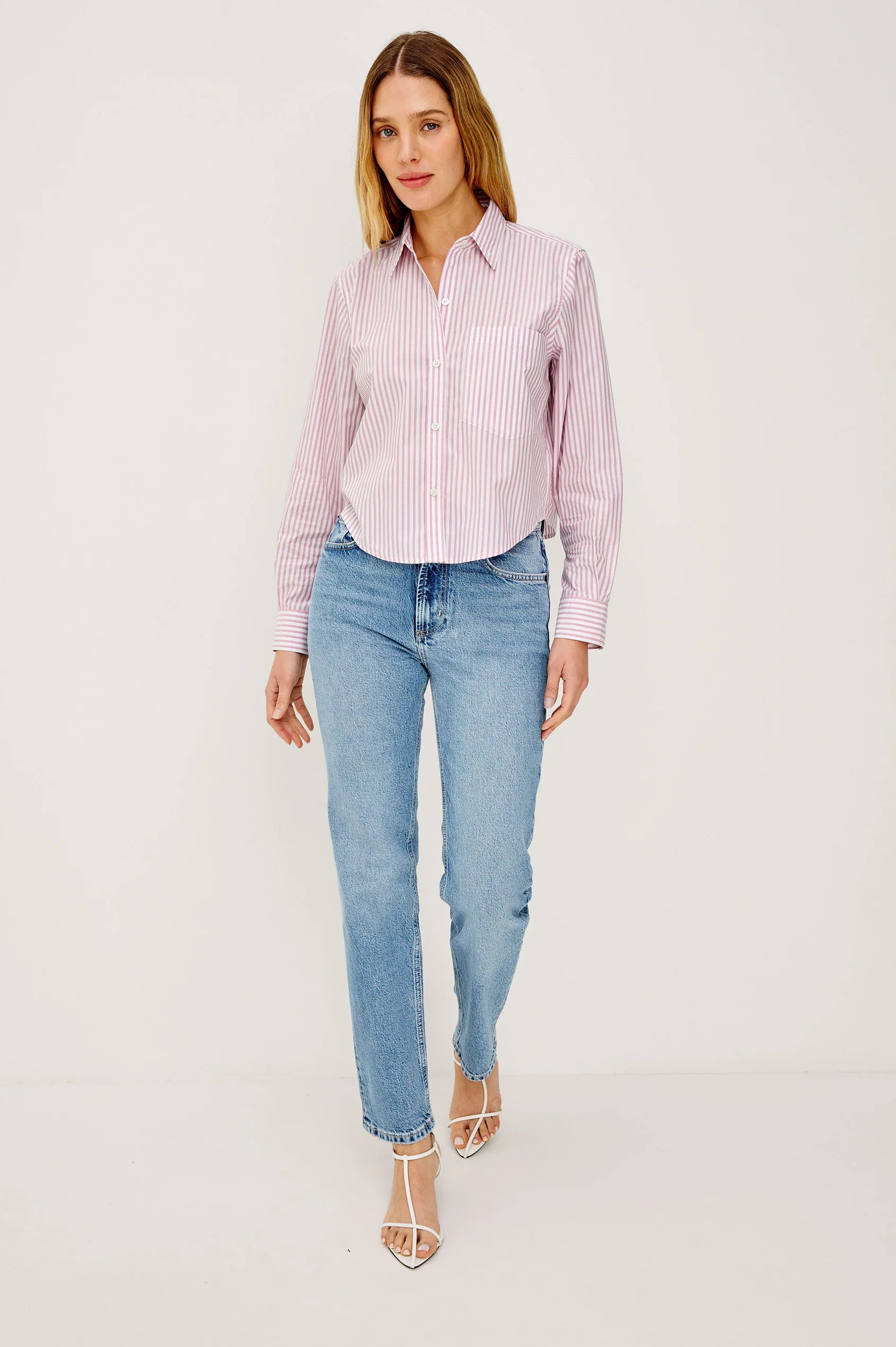 Woman wearing a pink and white striped shirt and light blue jeans on a white background