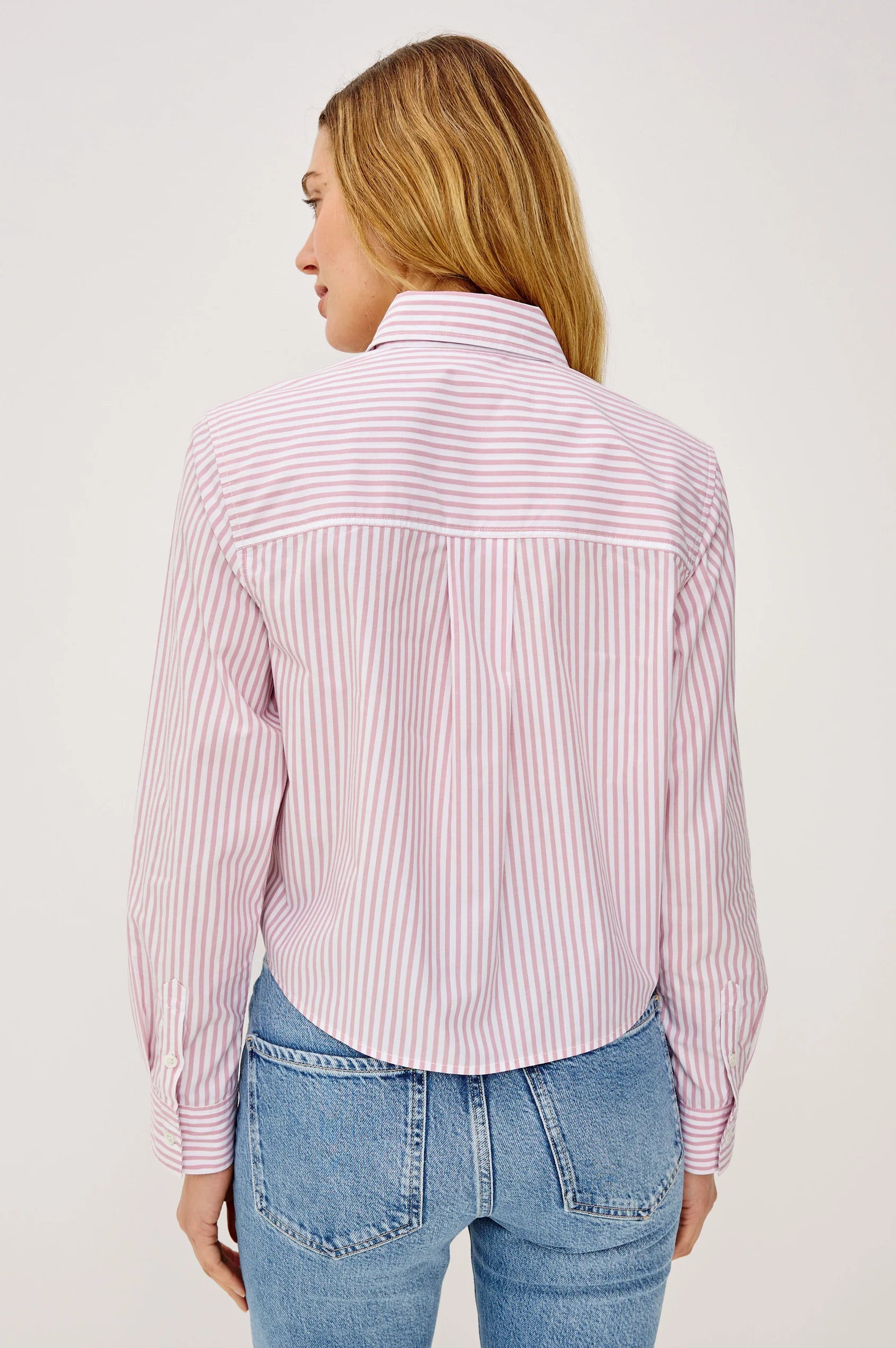 Woman wearing a pink and white striped shirt with blue jeans on a plain background