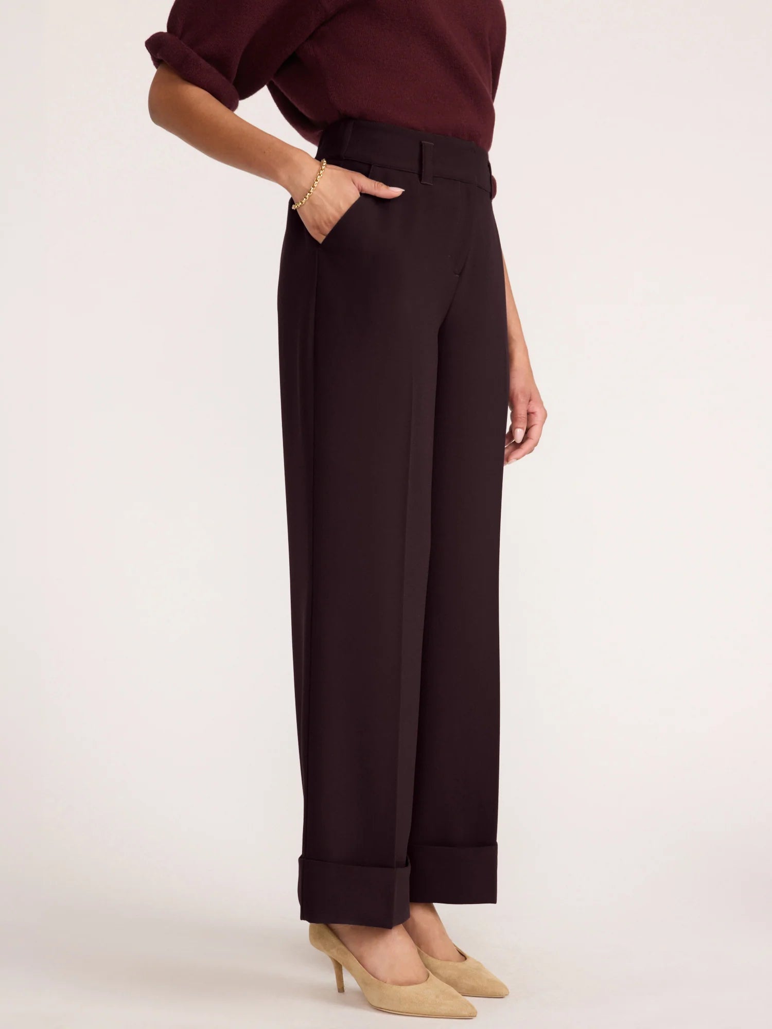 A model wearing dark brown wide-leg cropped trousers with a rolled waistband, paired with a dark burgundy top and beige heels, shown from the waist down against a light studio background.