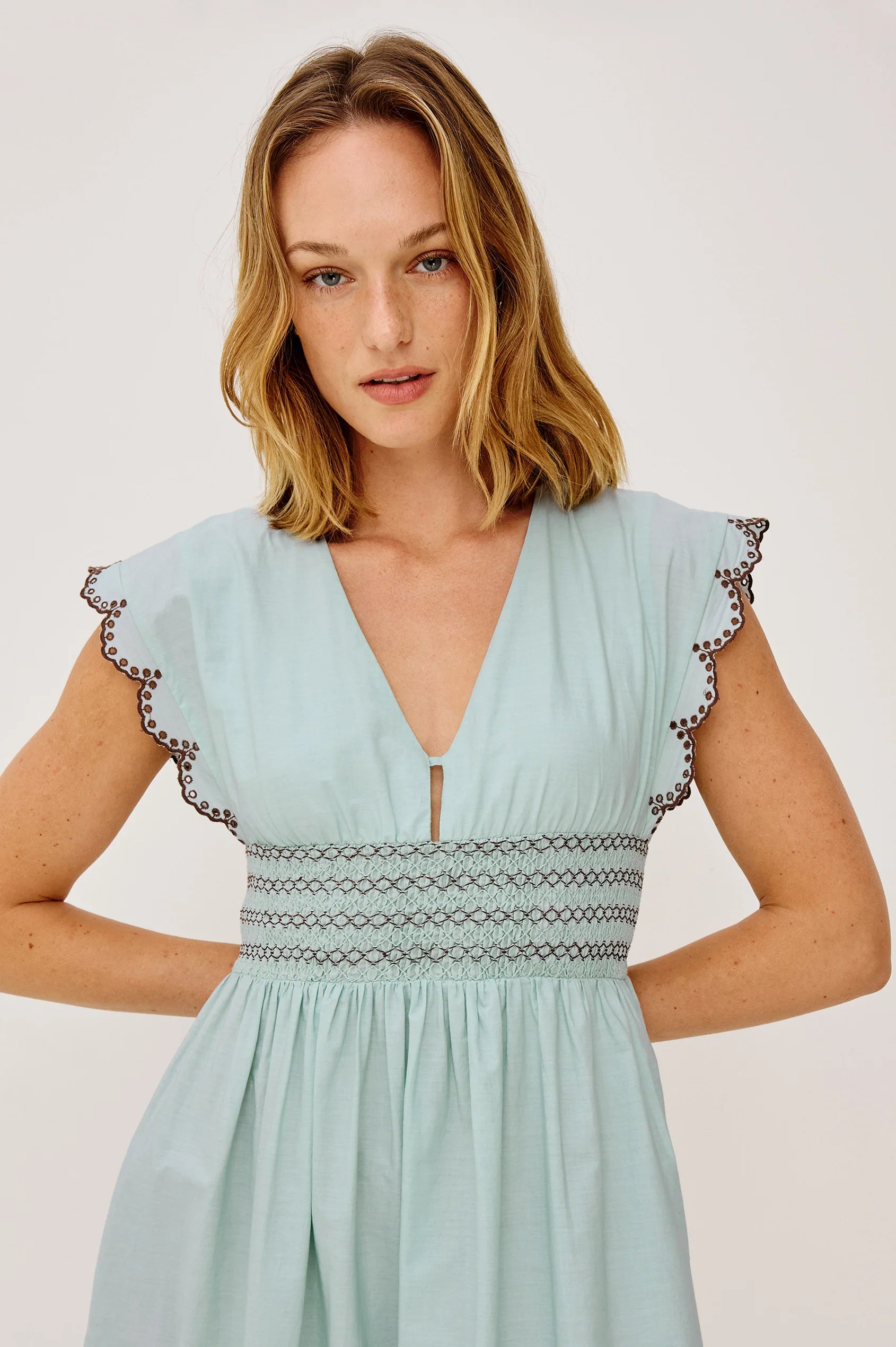 Woman wearing a light blue dress with lace details on a white background