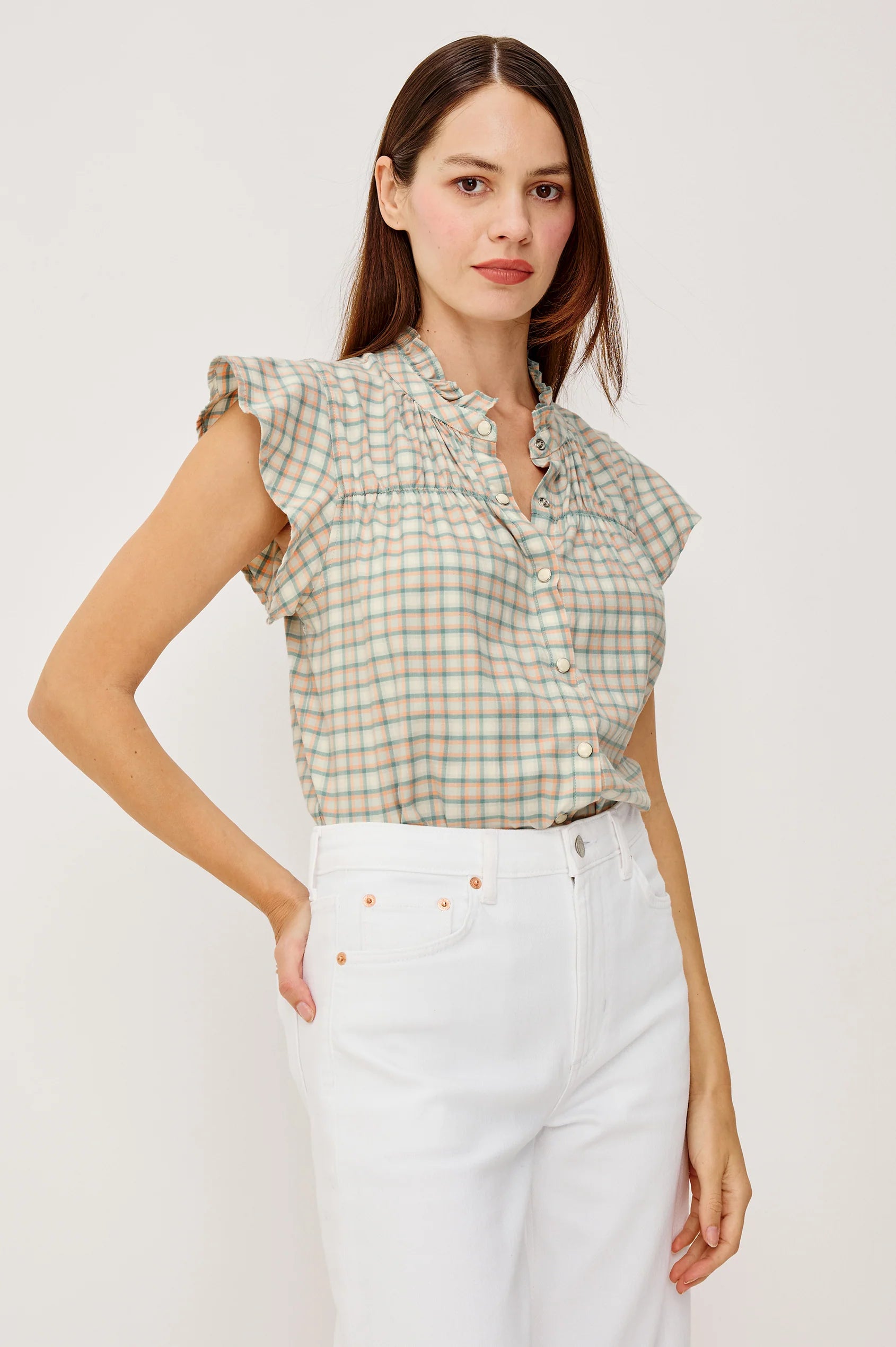 Woman wearing a checkered top and white pants against a plain background