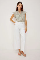Woman wearing a green checkered blouse and white pants on a plain background