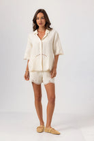 Woman wearing a cream-colored outfit with a matching shirt and shorts on a white background