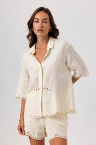 Woman wearing a white outfit with lace details on a plain background