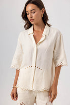 Woman wearing a white embroidered outfit against a plain background