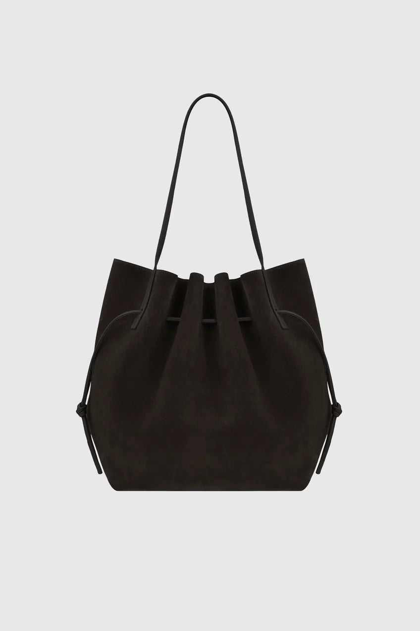A black suede bucket bag with a single shoulder strap, shown against a light gray background.