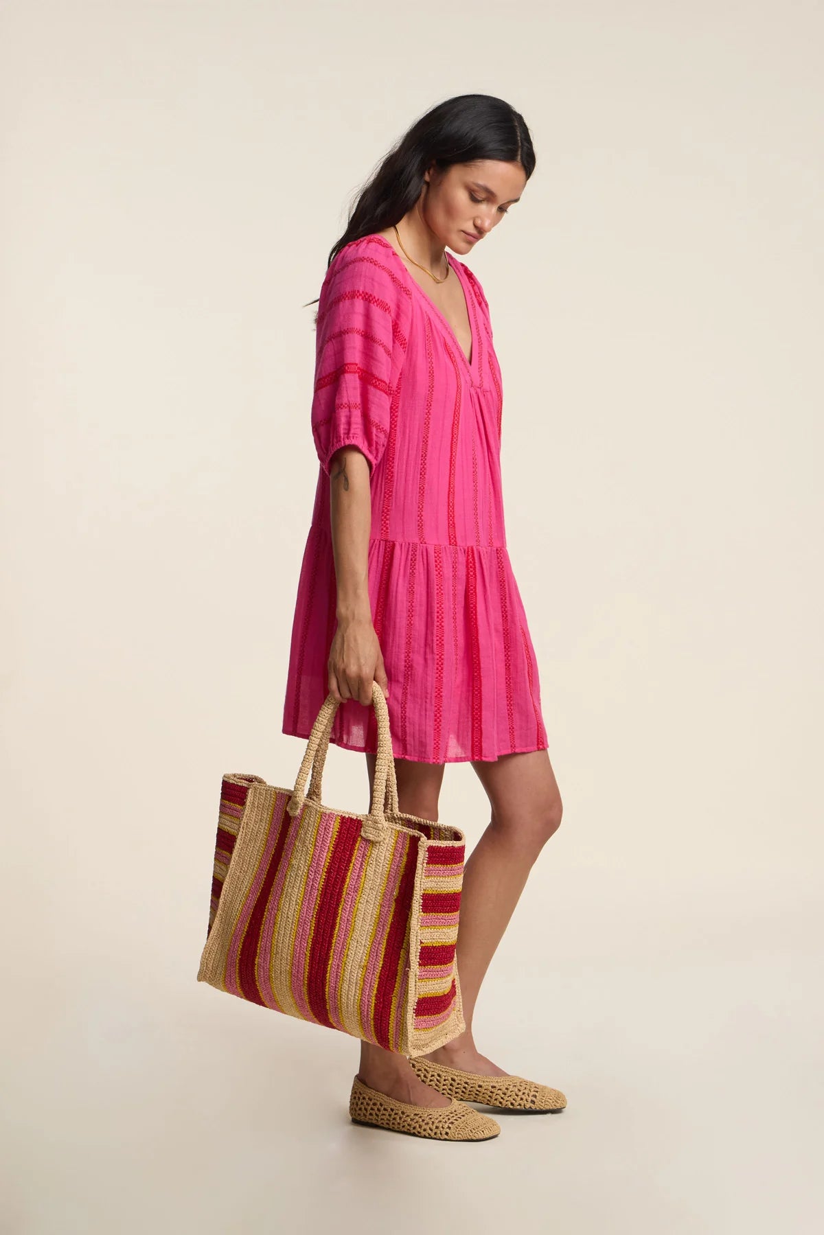 Woman in a pink dress holding a striped bag on a beige background