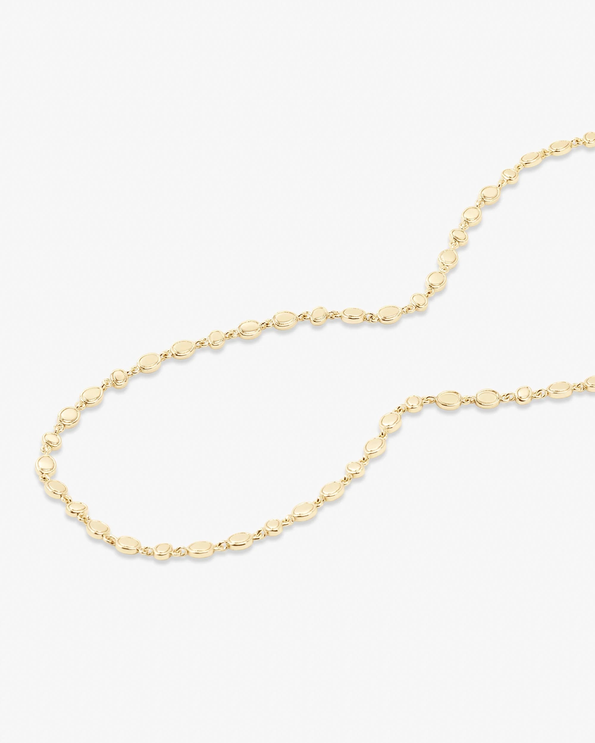 A delicate gold chain necklace with elongated oval links, arranged in a loose curve on a clean white background.